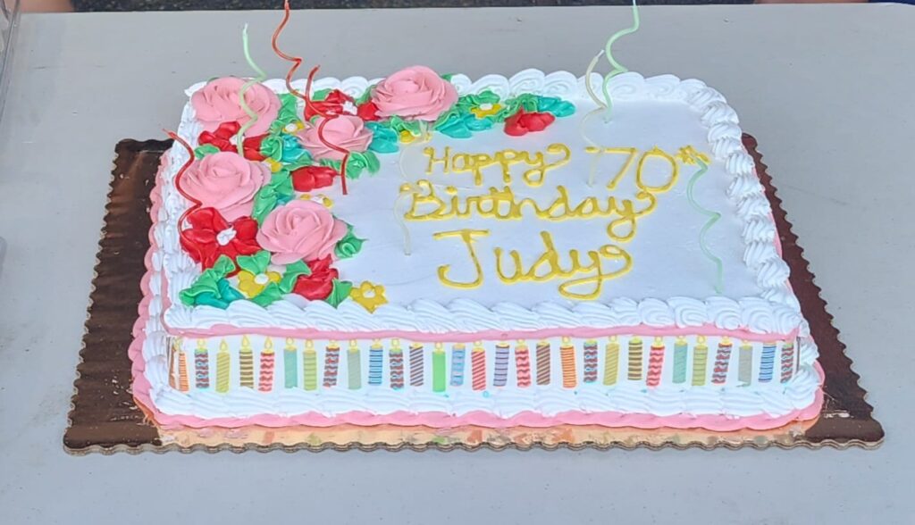 Judy Hoarfrost’s 70th birthday cake with pink and red frosting flowers
Caption: Judy's 70th birthday cake, beautifully decorated and surrounded by friends.